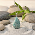 Amazonite pendant necklace on a chain with stones and bamboo leaves in the background