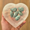 Heart-shaped selenite bowl with green-bluestones on a blurred background