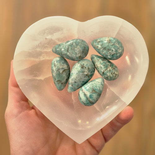 Heart-shaped selenite bowl with green-bluestones on a blurred background