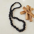 Black beaded necklace with palo santo sticks on a beige background