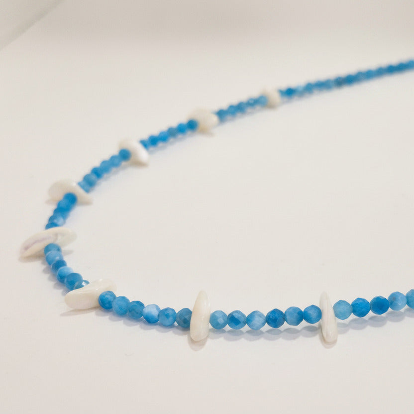 A beaded necklace featuring small round blue beads and irregular white shell-like accents, displayed against a plain light background.