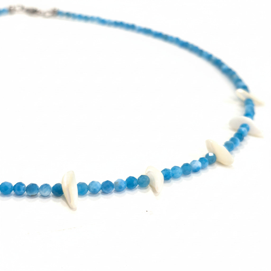 A beaded necklace with faceted blue beads and white shell-like accents, displayed on a white surface.