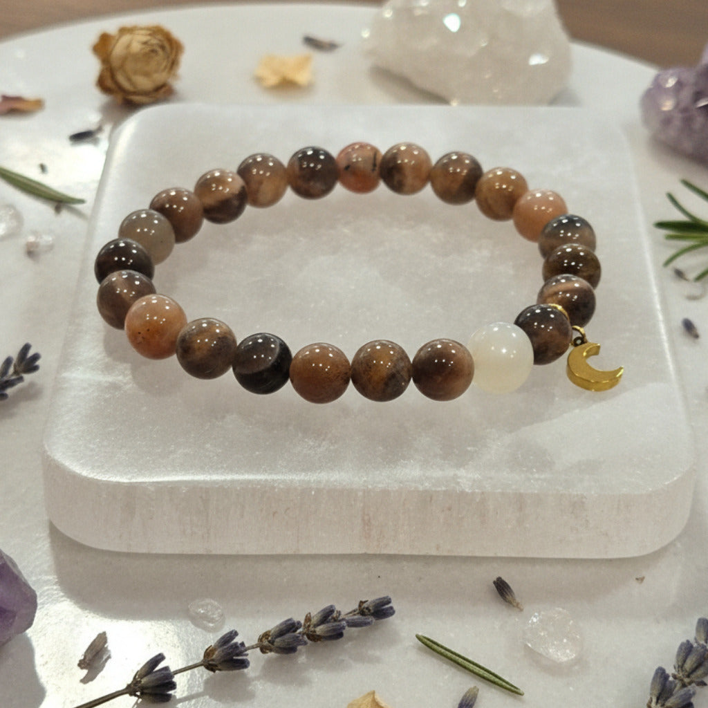 Beaded bracelet on a white selenite charging plate surrounded by herbs and crystals