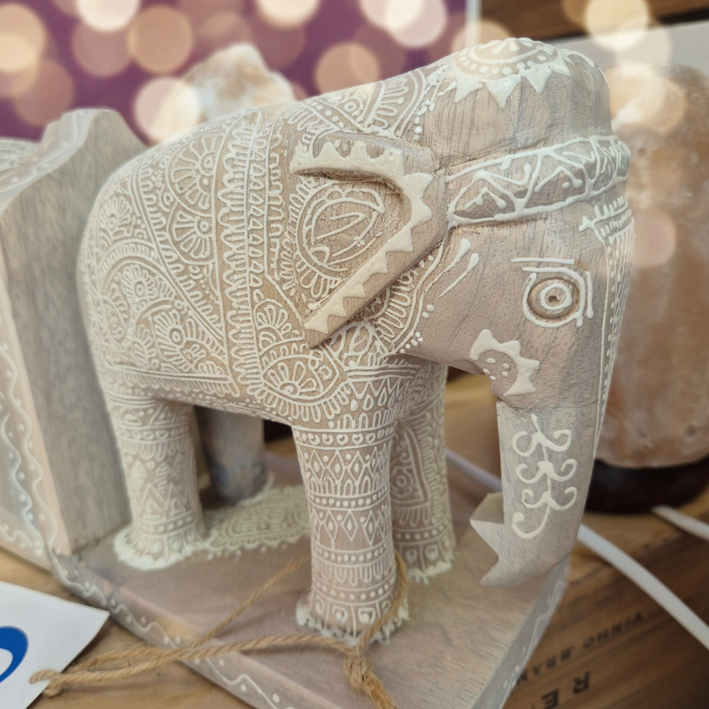A hand-carved wooden elephant figurine with intricate white painted patterns, displayed on a shelf.