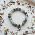 Beaded bracelet with a silver charm on a white surface with seashells and dried flowers