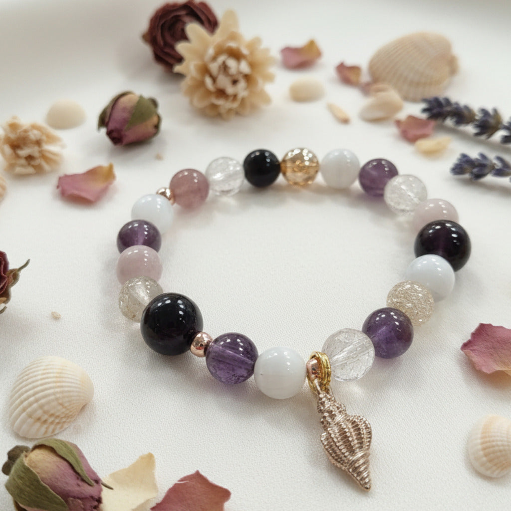 colorful beaded bracelet  with a gold seashell charm on a white surface with dried fliers and seashells around