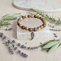 Multicolored beaded bracelet with a silver wing charm on a clear stone block, surrounded by lavender and greenery.