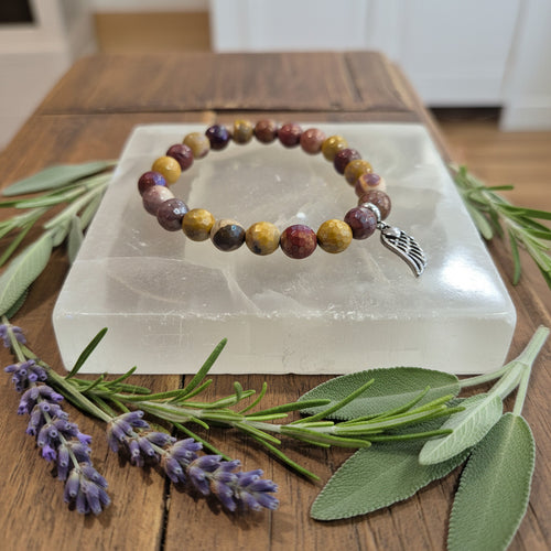 Multicolored beaded bracelet with a silver charm on a white stone surface, surrounded by greenery and lavender.