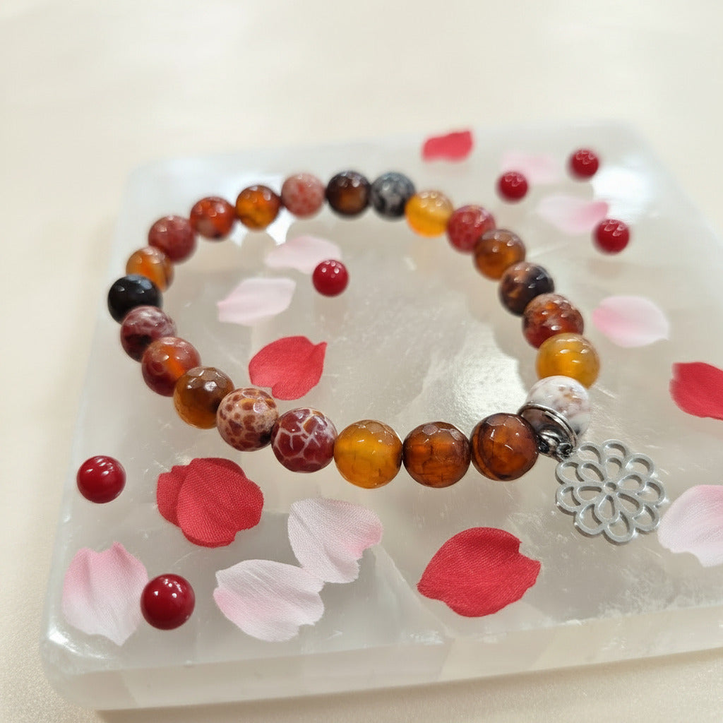 Beaded bracelet with a silver charm on a white stone surface with pink petals
