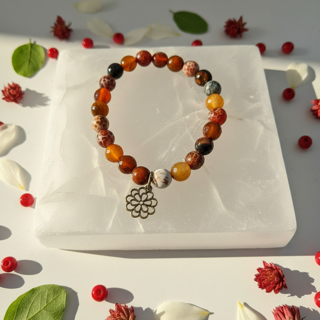 Multicolored beaded bracelet with a flower charm on a white stone surface surrounded by decorative leaves and flowers.