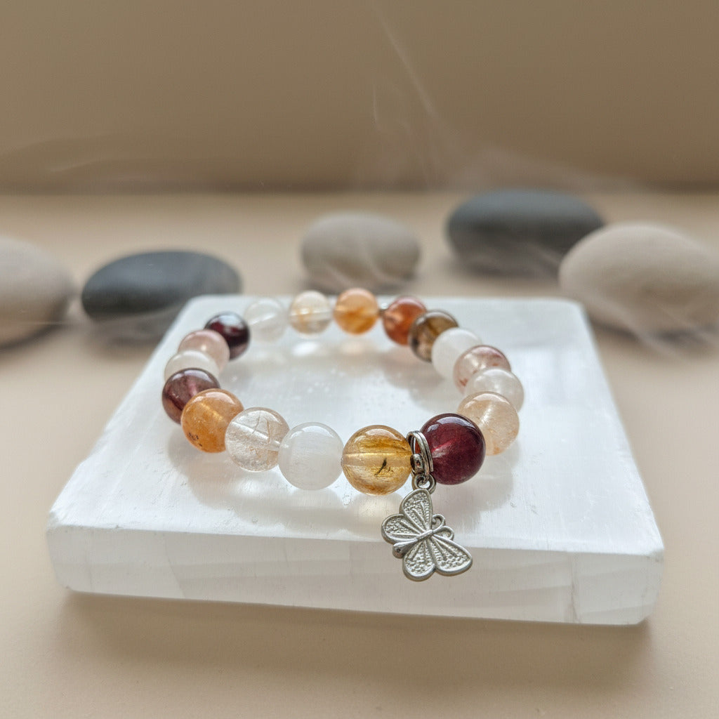 Multicolored beaded bracelet with a silver butterfly charm on a white stone surface with stones in the background.