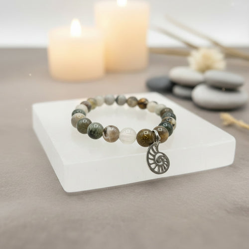 Beaded bracelet with a silver charm on a white stone surface with candles and stones in the background