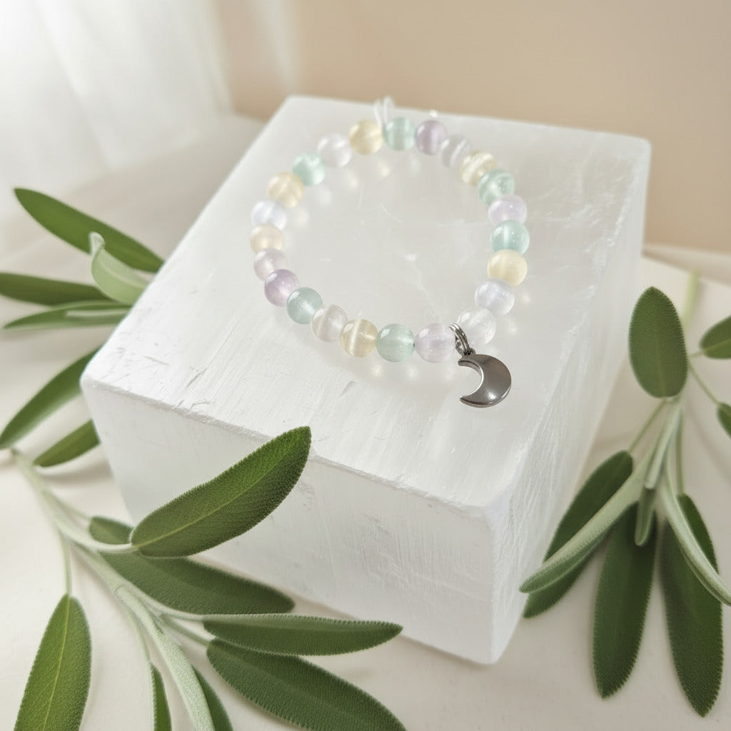 Beaded bracelet with a moon charm on a white box, surrounded by green leaves.
