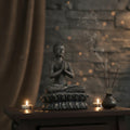 Buddha statue with incense and candles on a wooden table against a stone wall background