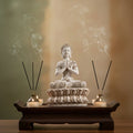 Buddha statue with incense sticks and candles on a wooden platform against a blurred background