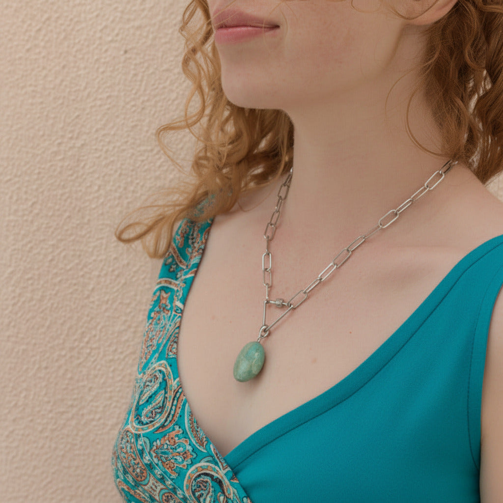 Woman wearing a turquoise top and a necklace with a amazonite pendant against a beige wall.