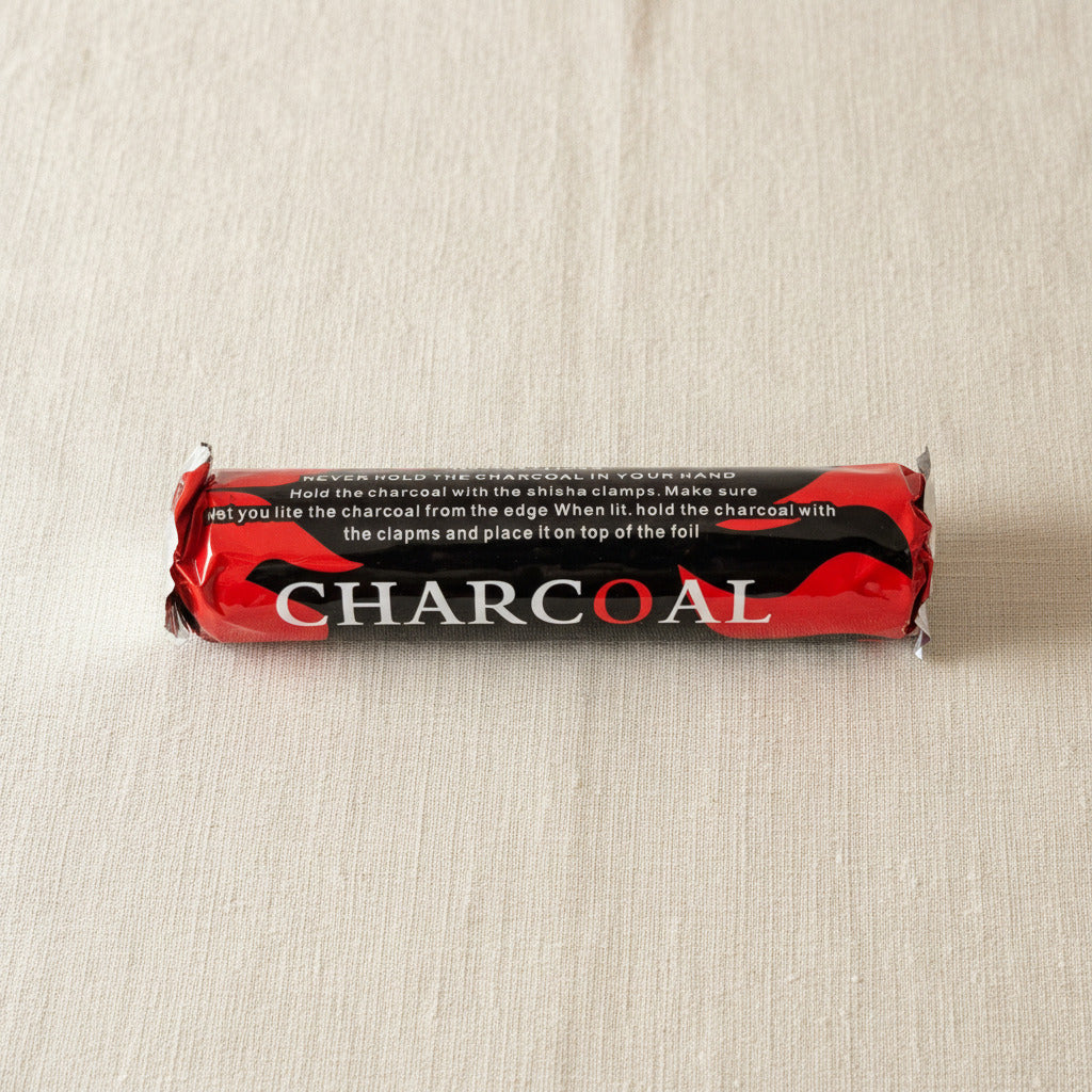 A packaged roll of charcoal with red, black, and white labeling showing safety instructions, photographed upright against a light neutral background.