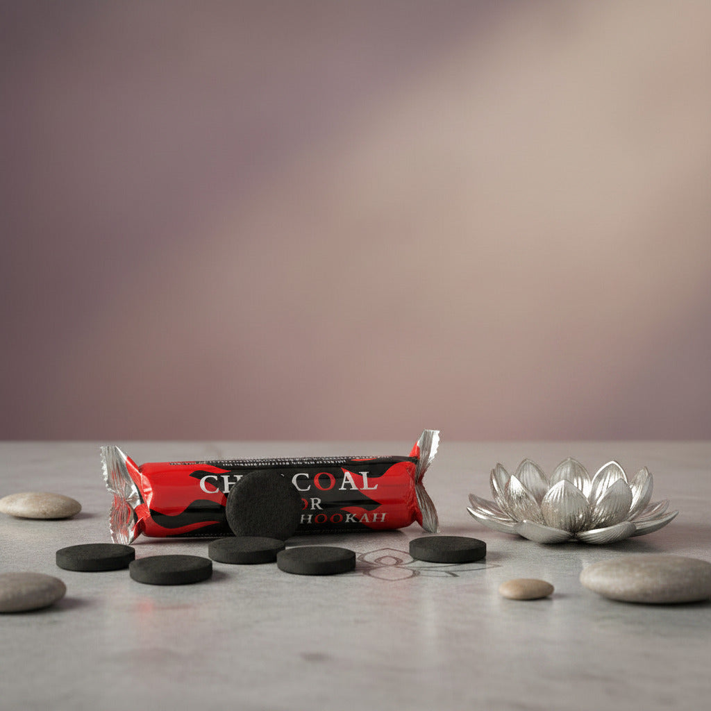 A packaged bar of charcoal hookah fuel wrapped in red, black, and white foil, placed next to a beige incense burner with cone incense burning on a light beige surface with stones around