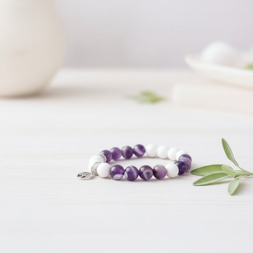 Beaded bracelet with purple and white beads on a light surface with a leafy branch.