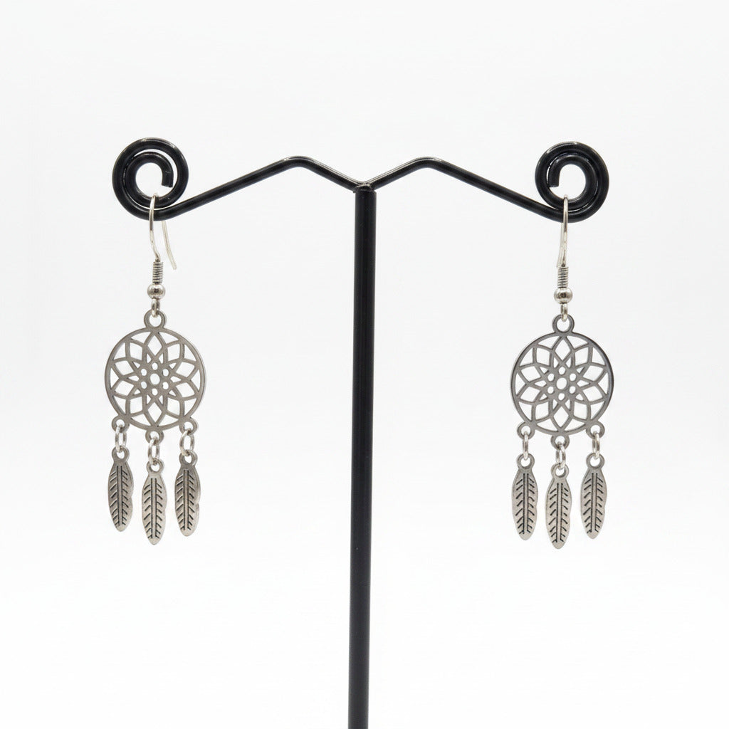 Pair of silver dreamcatcher earrings on a black stand against a beige fabric background