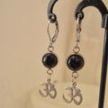 Silver color earrings with black stones and decorative elements on a beige background