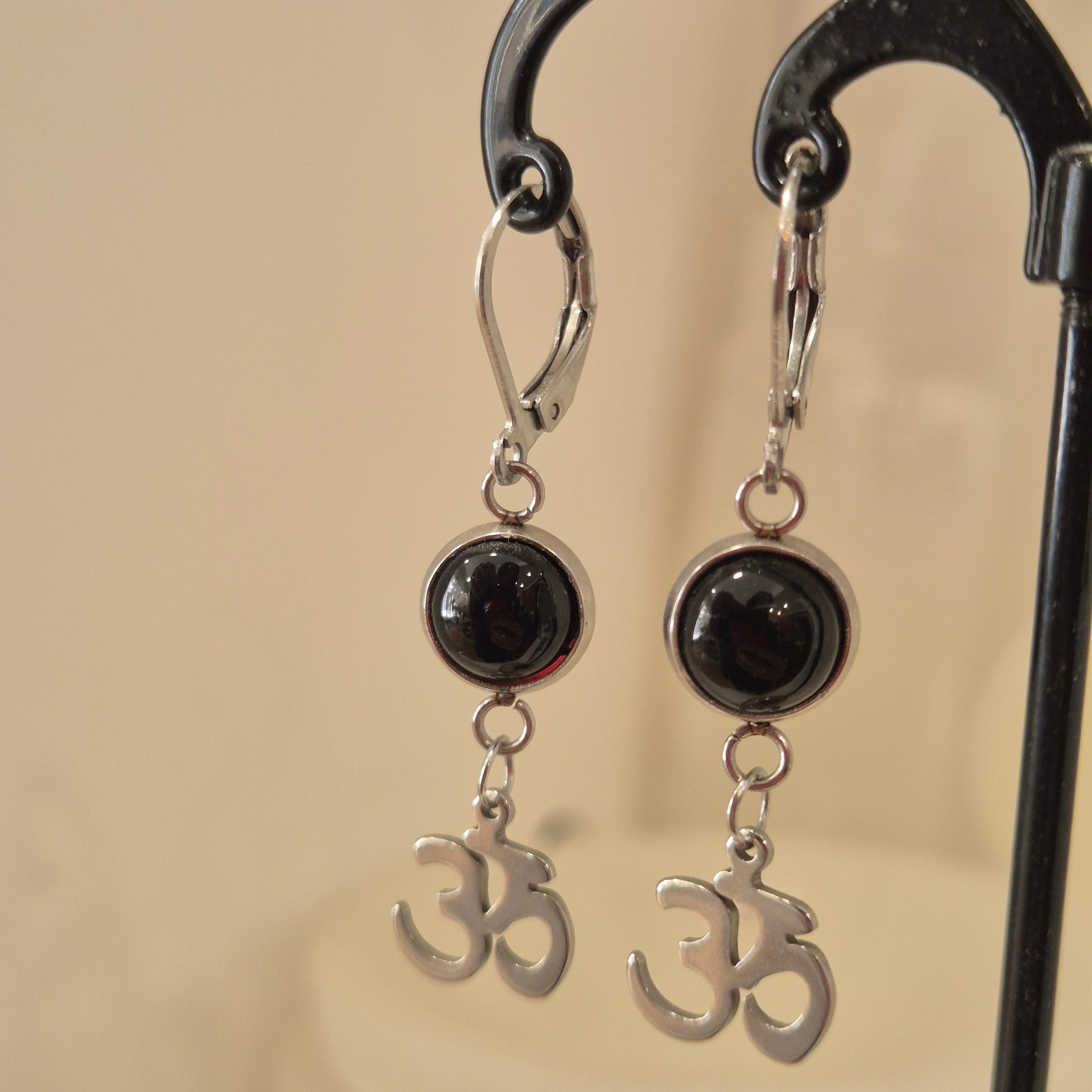 Silver color earrings with black stones and decorative elements on a beige background
