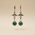 Pair of earrings with natural malachite and angel charm and silver hooks on a beige background