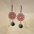 Pair of earrings with red floral designs and green stones on a beige background