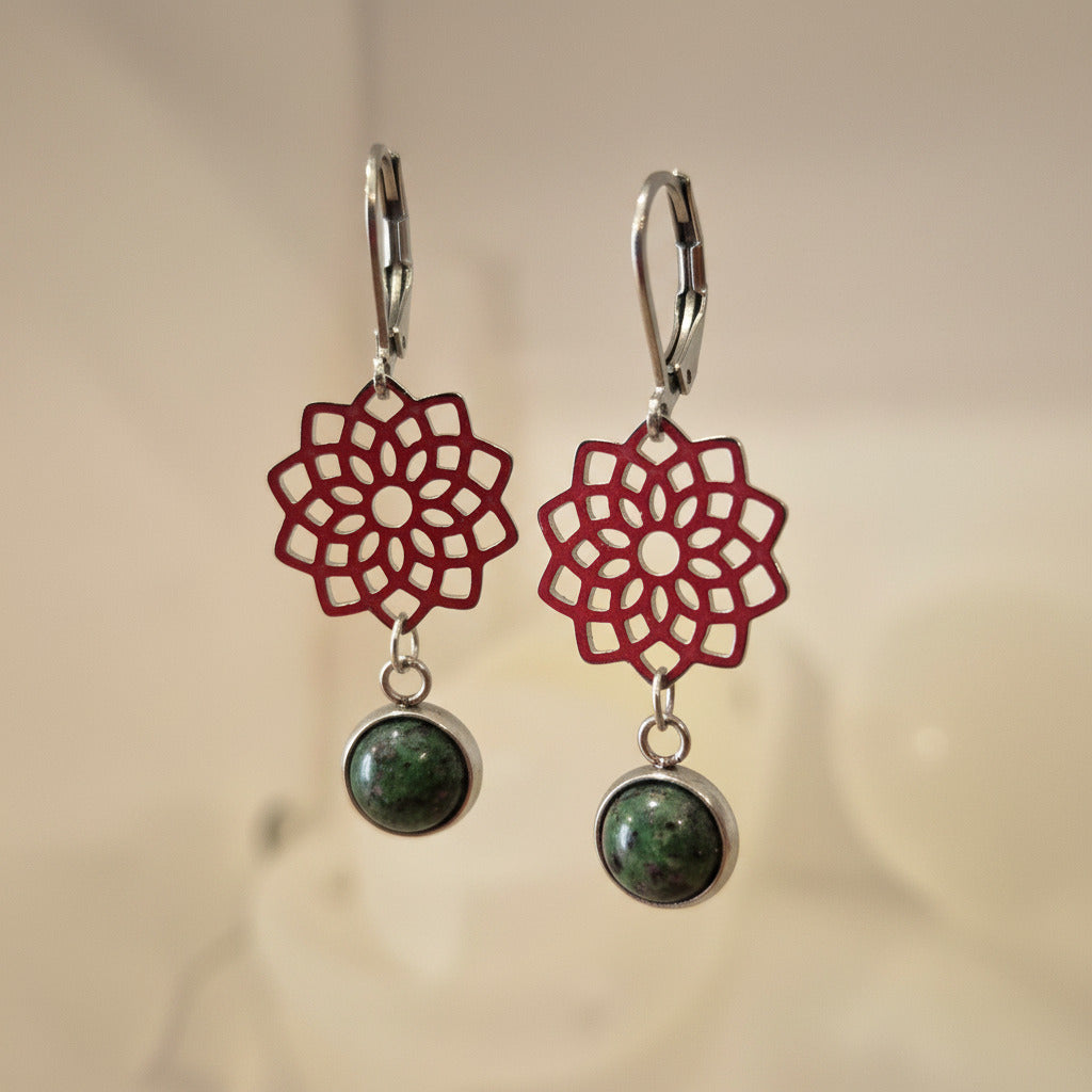 Pair of earrings with red floral designs and green stones on a beige background