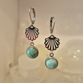 Pair of earrings with shell-shaped top and round gemstone bottom on a soft background