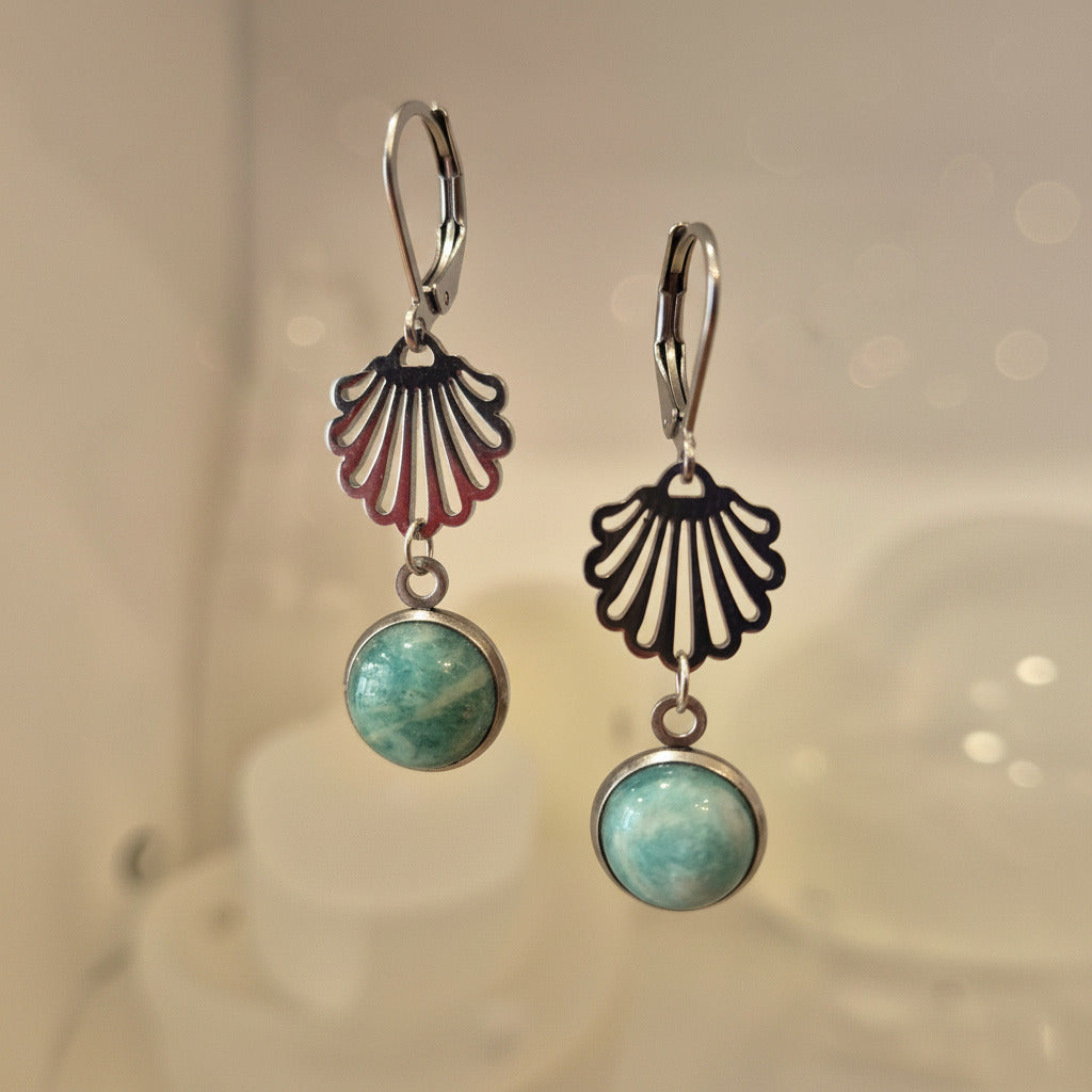 Pair of earrings with shell-shaped top and round gemstone bottom on a soft background