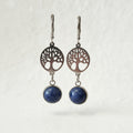 Pair of earrings with tree-of-life design and blue stones on a neutral background
