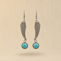 Silver wing-shaped earrings with turquoise stones on a beige background
