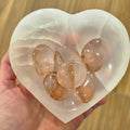 Heart-shaped selenite bowl with hematoid quatz stones held by a hand.