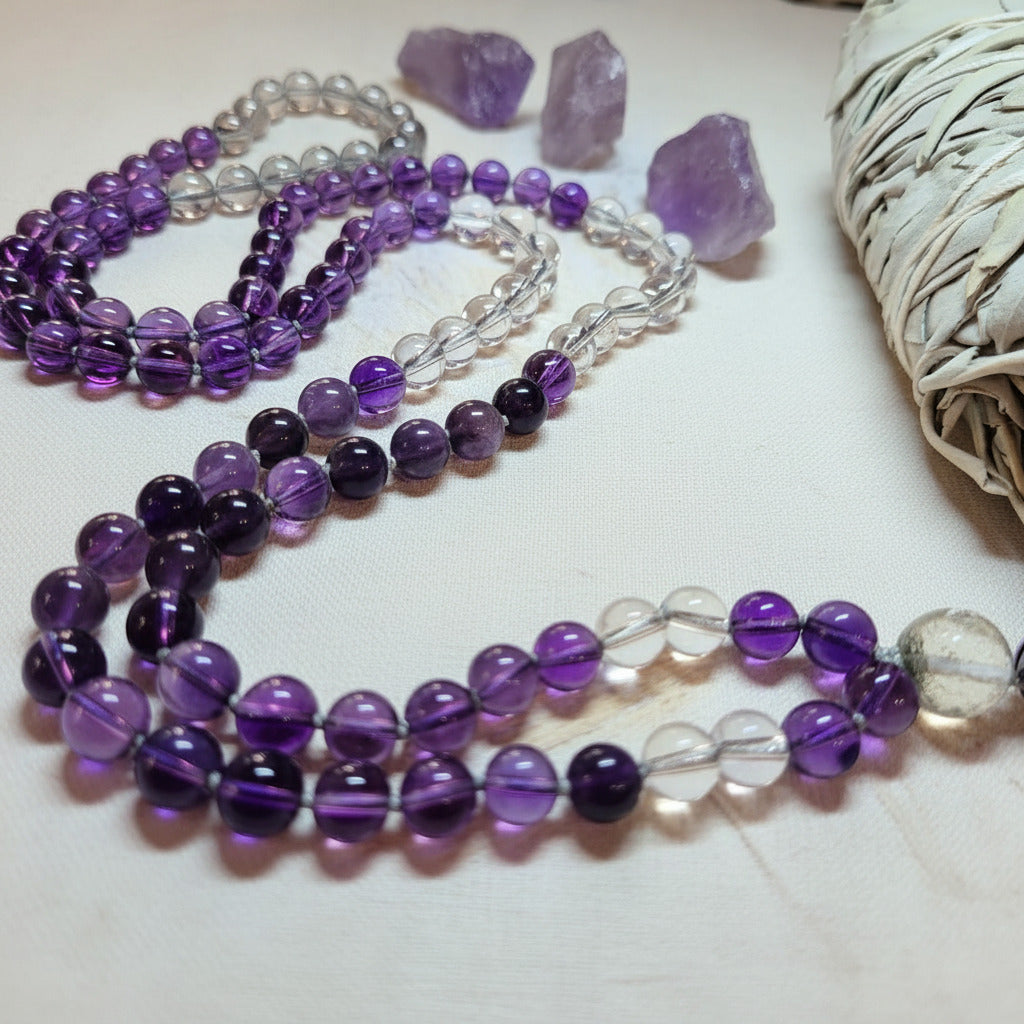 Purple and clear beaded necklace on a light surface with amethyst stones.