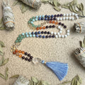 Colorful beaded necklace with a blue tassel on a beige surface with dried leaves and smudge sticks.