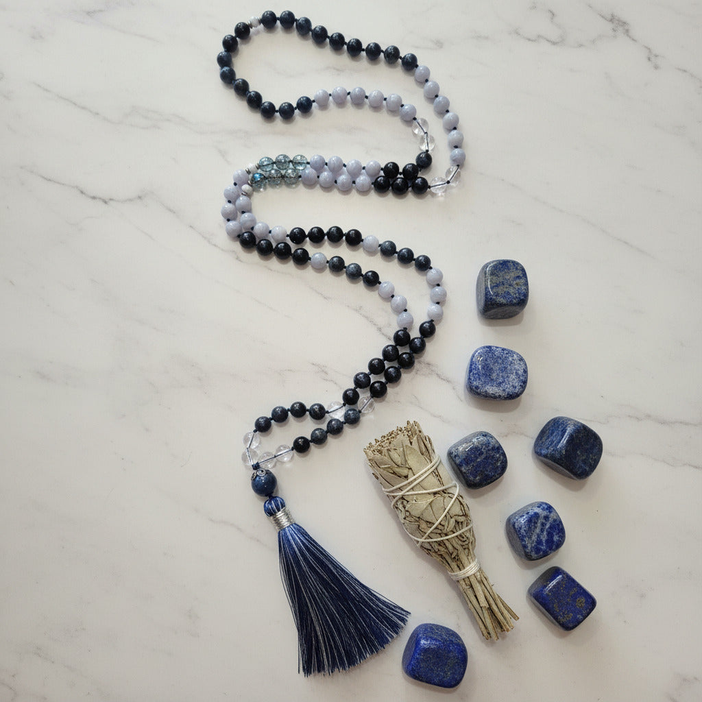 Beaded necklace with tassel, sage bundle, and lapis stones on a marble surface
