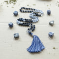 Meditation beads with a blue tassel on a textured beige surface