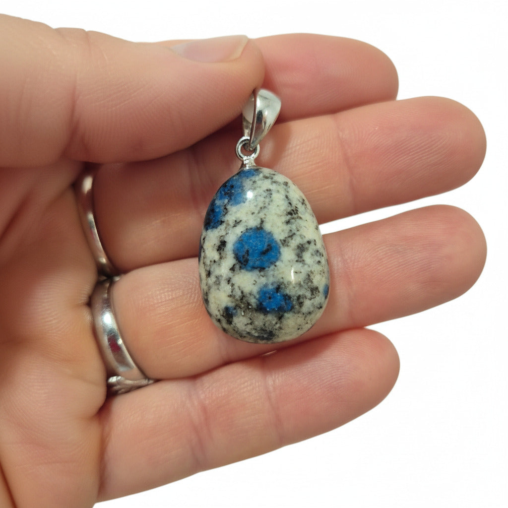 Hand holding a pendant with a blue and gray stone, white background