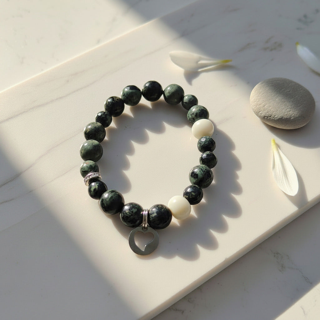 Green and white beaded bracelet on a marble surface with a stone and flower petals.