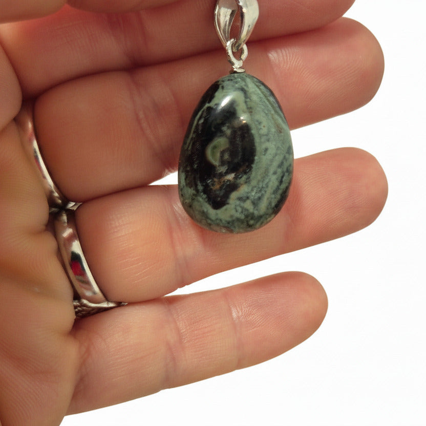 Hand holding a pendant with a stone-like design against a blurred background of stones.