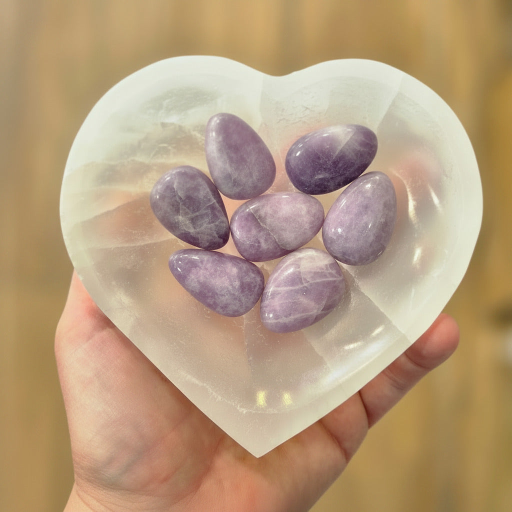 Heart-shaped crystal dish with purple stones held by a hand against a blurred background
