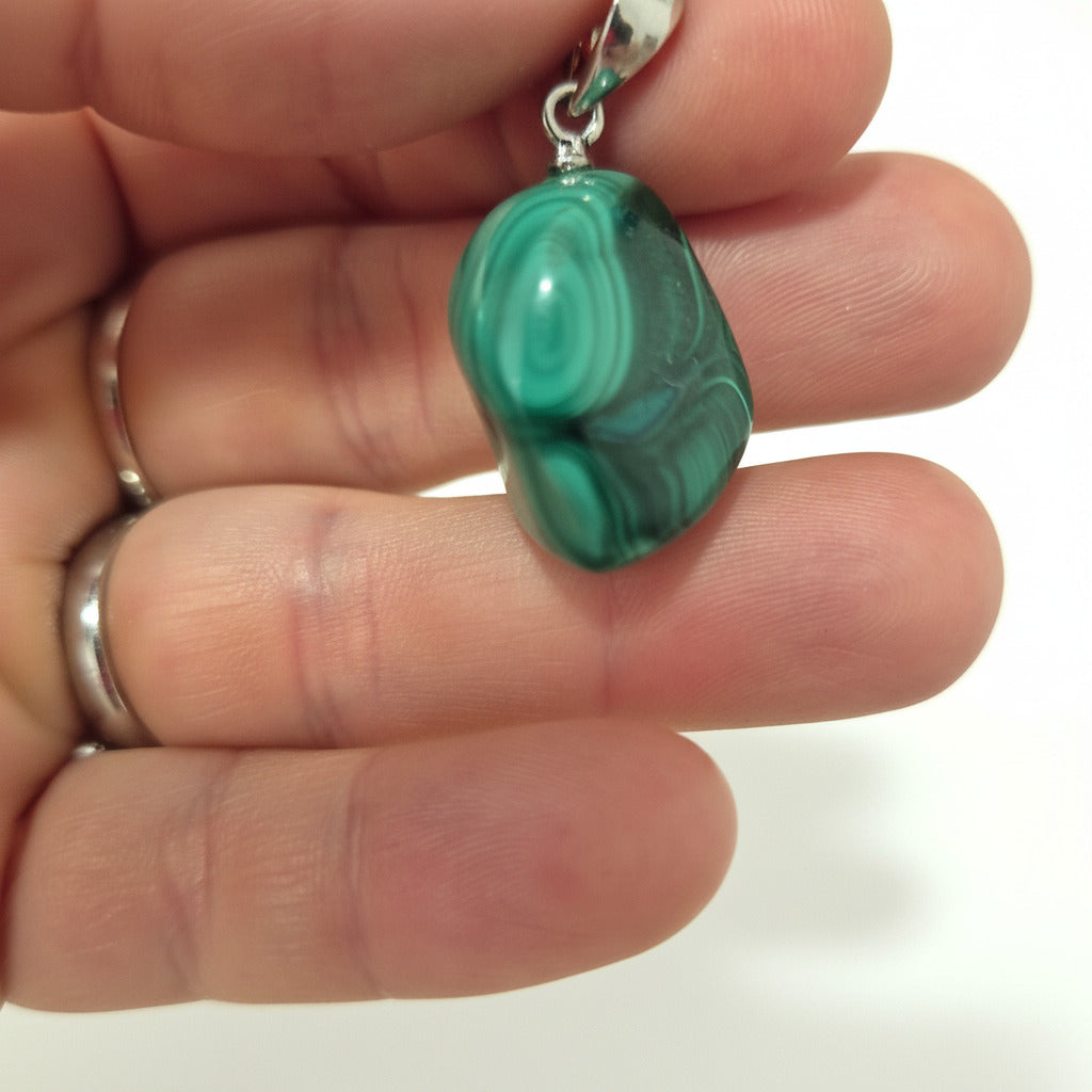 green malachite pendant held between fingers with white background