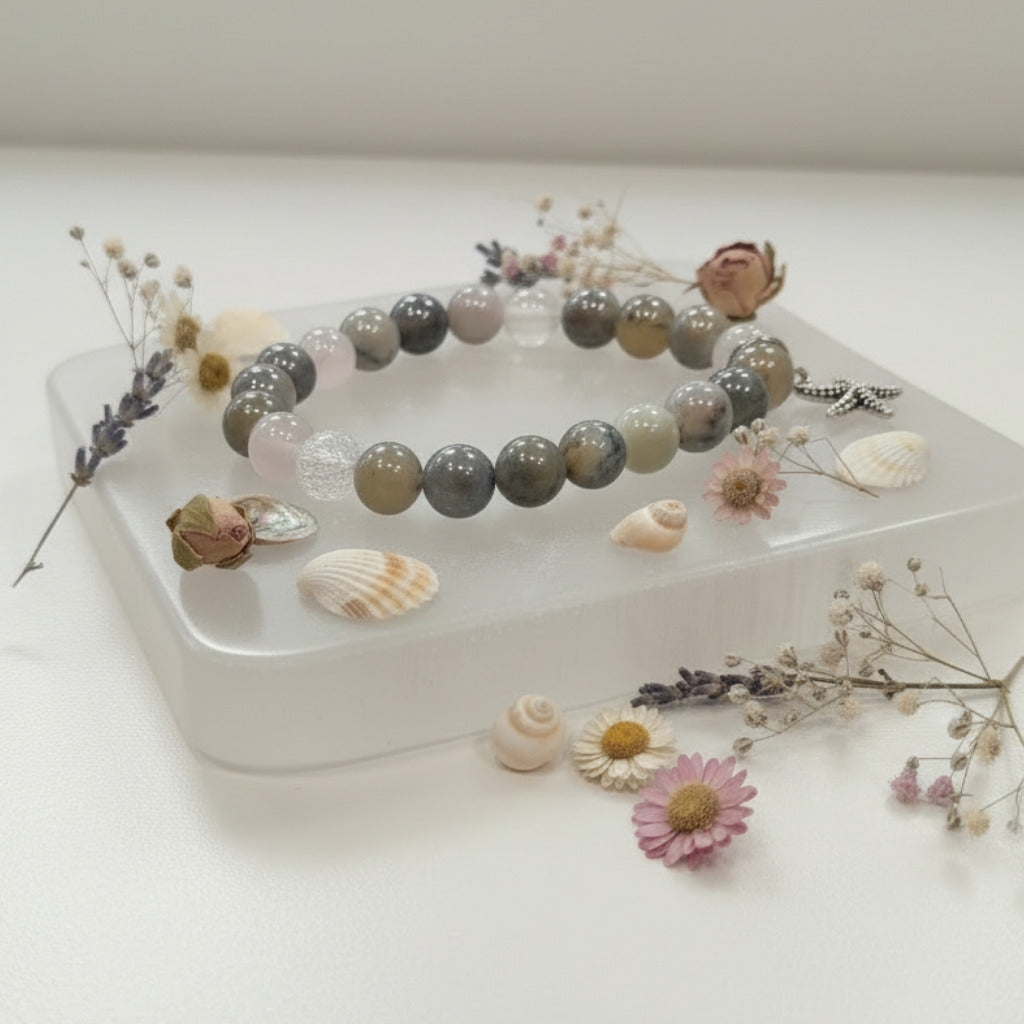 Grey beaded bracelet with starfish charm on a selenite stone over a white surface. Dried flower and seashell around