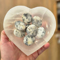 Heart-shaped selenite bowl  filled with white and gray palm stones held by a hand.