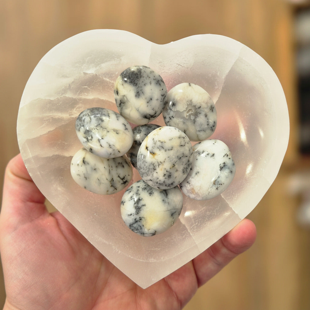 Heart-shaped selenite bowl  filled with white and gray palm stones held by a hand.