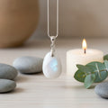 moonstone pendant hanging on chain with stones and a candle in the background