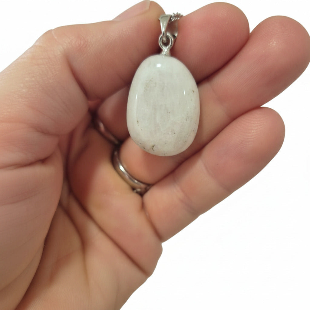 Hand holding a necklace with a white stone pendant against a blurred background
