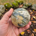 Hand holding a marbled stone with a natural background of rocks and leaves
