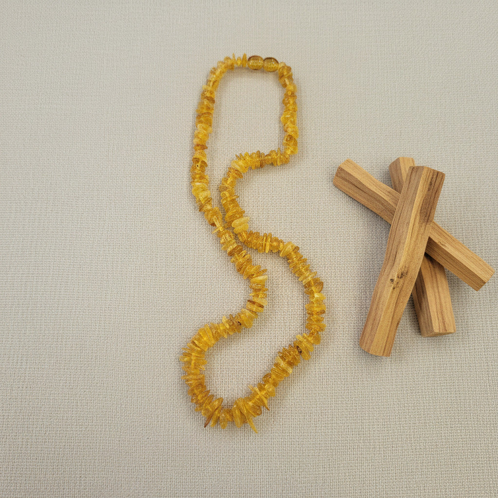 Yellow chip amber beaded necklace and wooden sticks on a beige fabric background